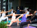 Yoga-/fitnessstudio met groep mensen die op yogamatten rek- en balanshoudingen doen, met waterflessen en gestapelde rekken op de achtergrond